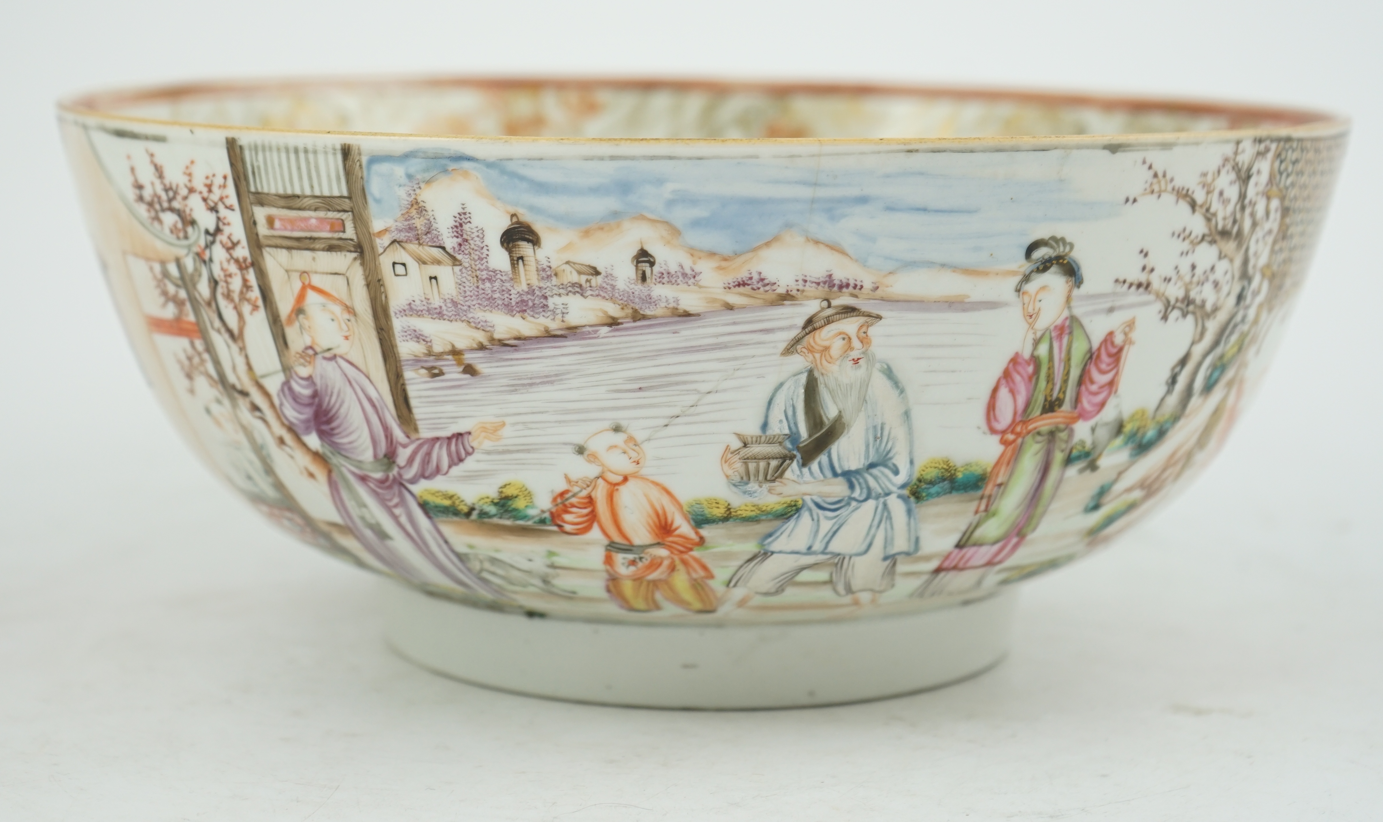 A Chinese famille rose ‘mandarin’ bowl, Qianlong period, painted with figures in a lakeside garden, between red enamelled landscape vignettes and cellular panels, 28.4cm diameter. Condition - there is a hairline crack to